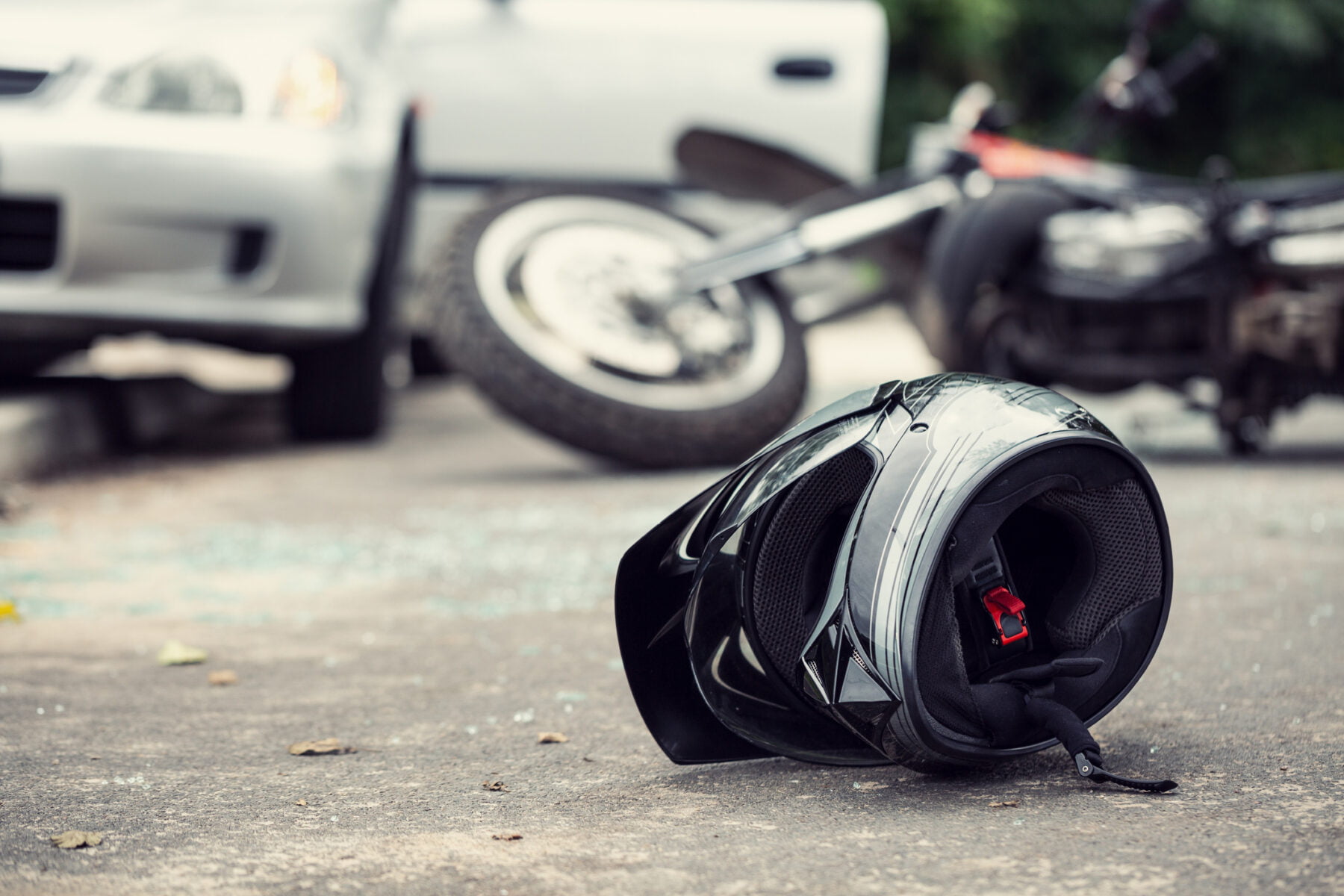 A motorcycle helmet is seen in the foreground with a fallen bike and a car in the background, clearly in the aftermath of a collision.
