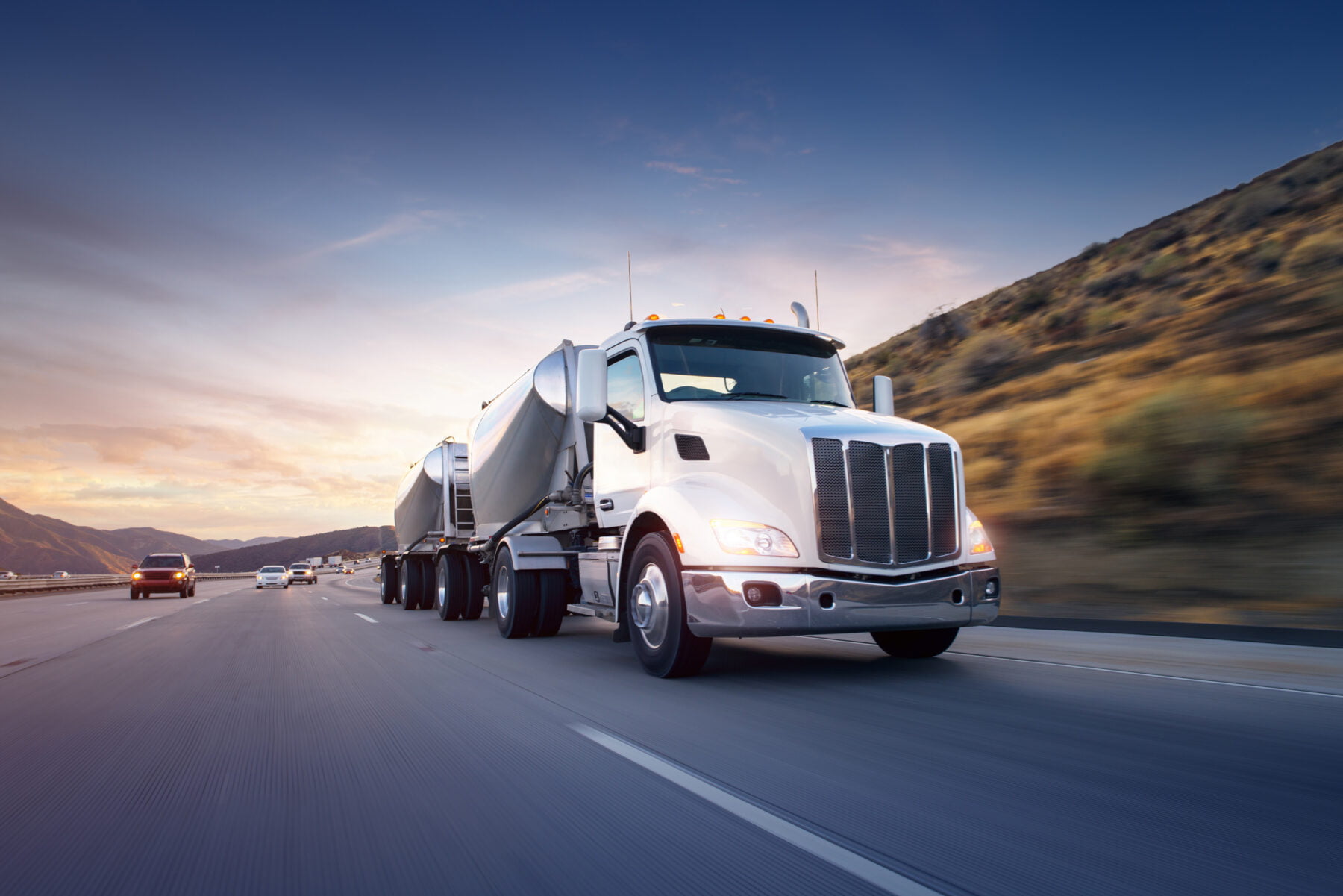 A truck driver speeds along the highway with the landscape in the background.