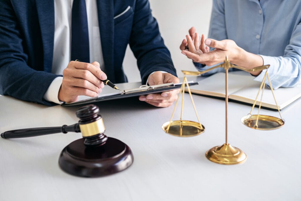 Two individuals in a legal consultation discussing documents, with a gavel and scales of justice on a desk.