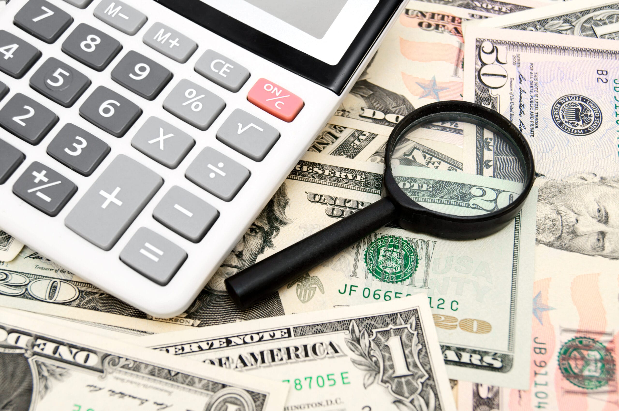 A calculator and magnifying glass placed on top of U.S. dollar bills.