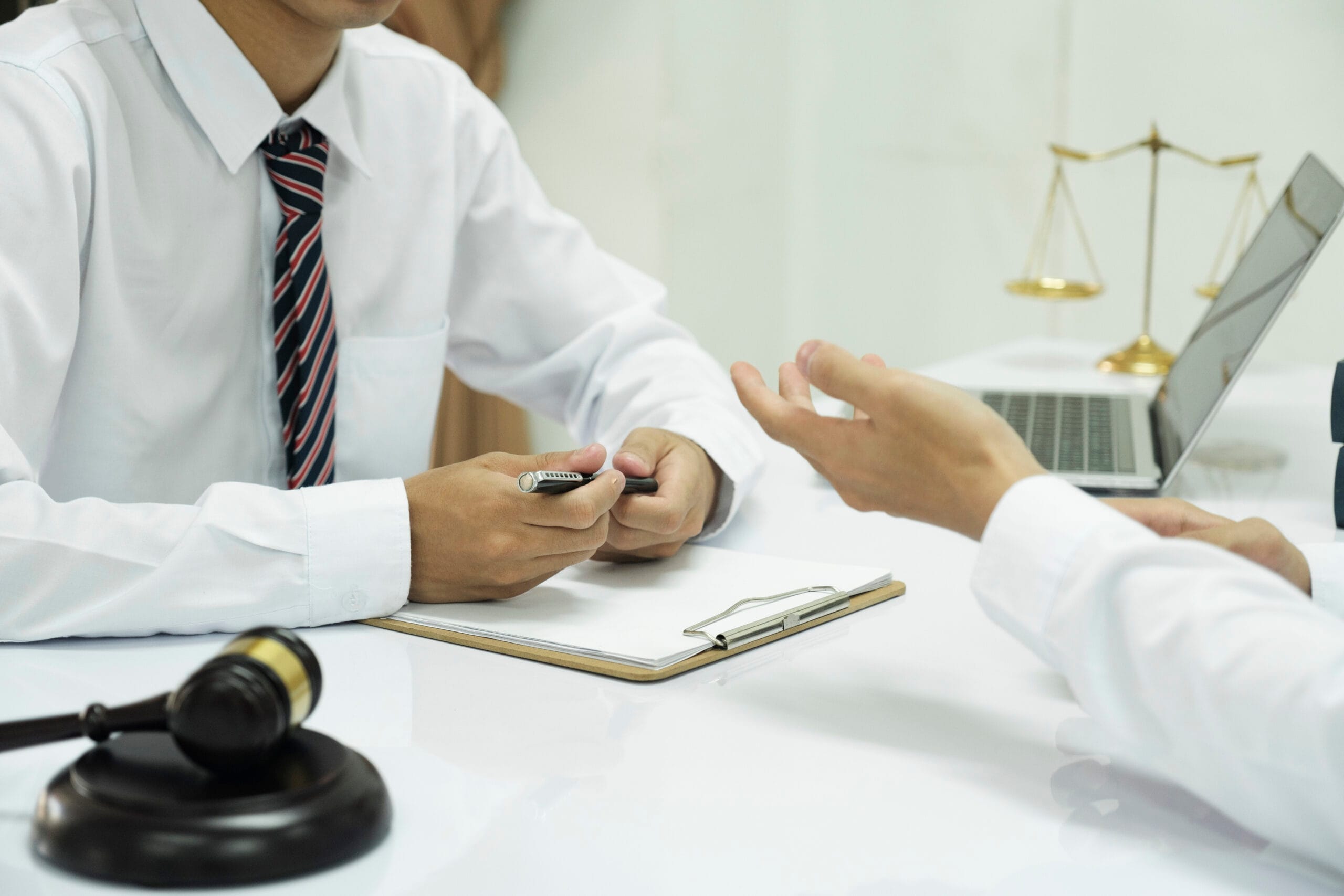 A lawyer and their client in a discussion across a desk with a clipboard, gavel, and scales of justice.