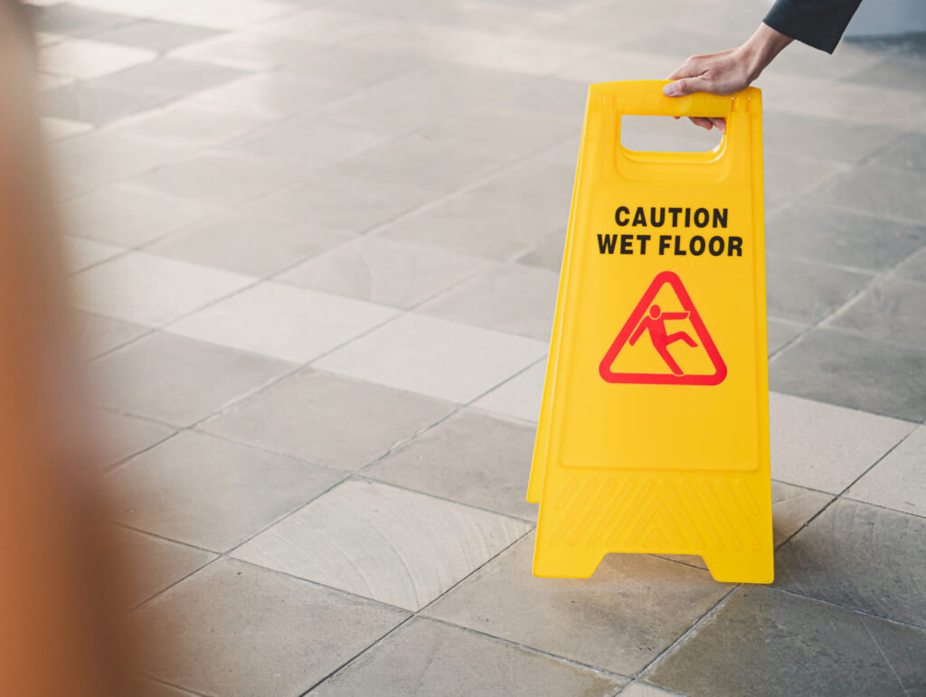 Yellow caution wet floor sign placed on a tiled surface with a person’s hand adjusting it.